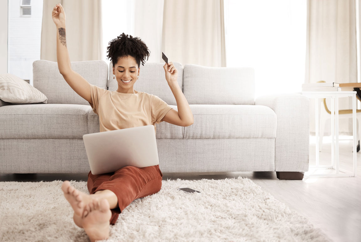 African American female sitting near couch and celebrating e-commerce purchase