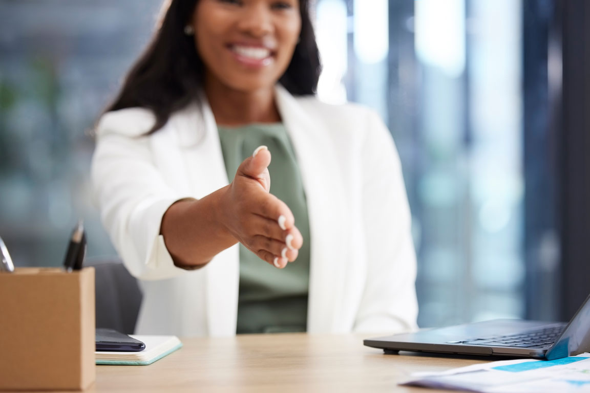 African American businesswoman putting hand across desk to shake hands